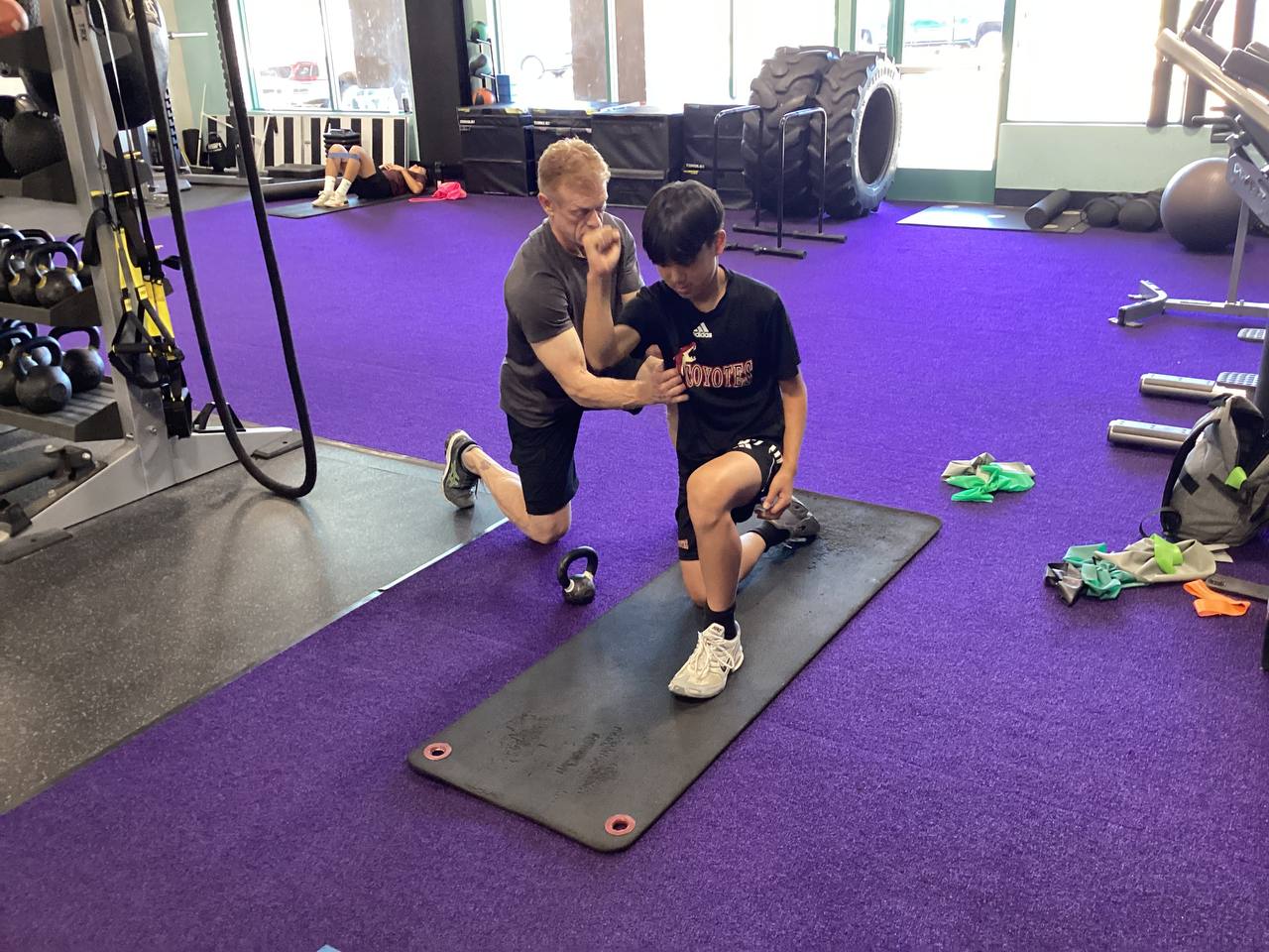 Robert kneeling on purple turf, coaching an athlete through a lunge